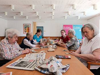 Gruppe von Bewohner*innen und Betreuungspersonen formt gemeinsam Papiermaché-Tiere aus Zeitung und Folie im Pflegewohnhaus.