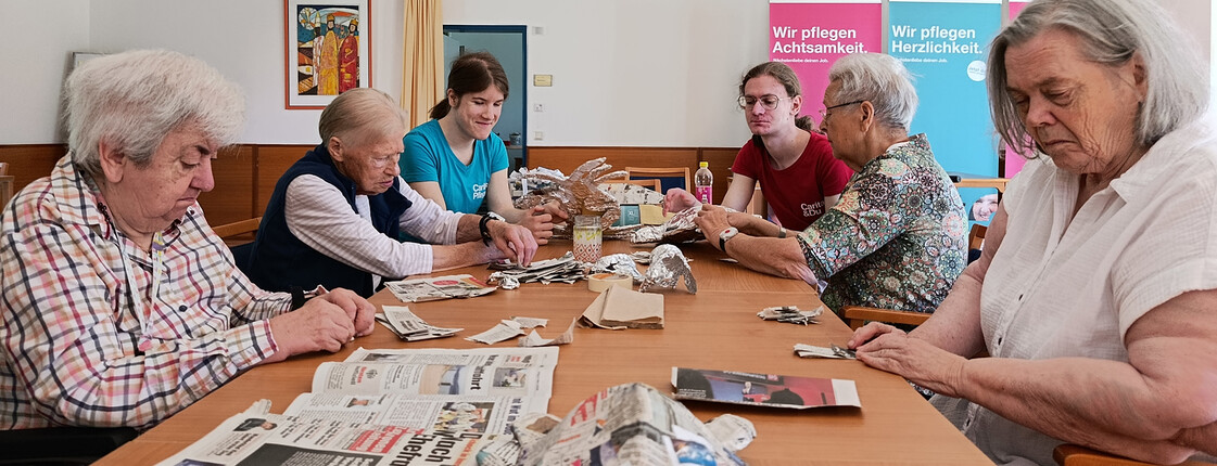 Gruppe von Bewohner*innen und Betreuungspersonen formt gemeinsam Papiermaché-Tiere aus Zeitung und Folie im Pflegewohnhaus.