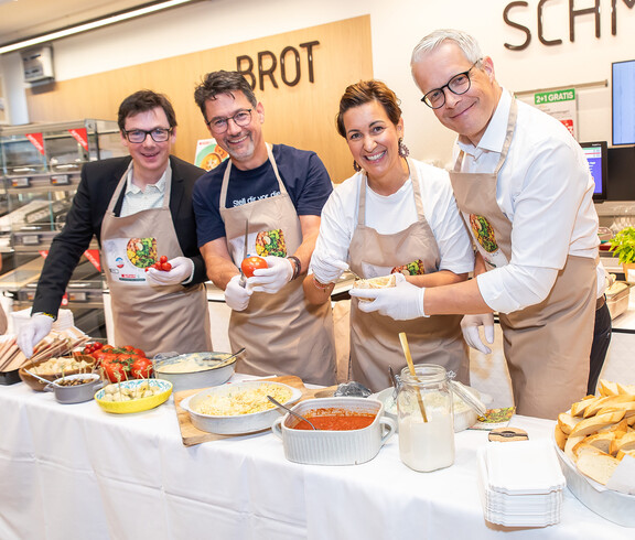 Vier Personen bereiten Speisen mit Tomaten und Brot bei Verkostung im SPAR-Supermarkt in Villach zu.