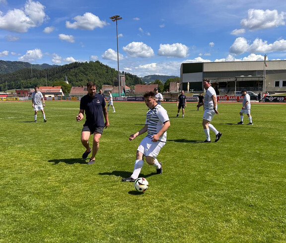 Teilnehmende spielen Fußball auf einem Sportplatz, im Hintergrund Tribüne und Landschaft beim Teamtag der Caritas Lebensgestaltung.