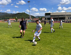 Teilnehmende spielen Fußball auf einem Sportplatz, im Hintergrund Tribüne und Landschaft beim Teamtag der Caritas Lebensgestaltung.
