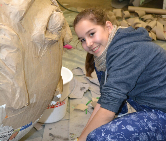 Eine Jugendbotschafterin mit langen braunen Haaren arbeitet an einer ihrer Figuren. Sie trägt ein blaues Oberteil und eine Hose. 