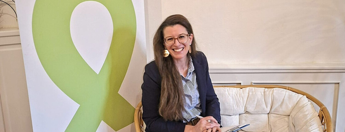 Elena Bucher, Absolventin des Caritas Lehrgangs Ehe- Familien- und Lebensberatung sitzt auf einer weißen Couch vor einem Rollup der "Aktion Leben".