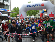 Eine große Ansammlung von Jugendlichen befindet sich in einer Innenstadt. Sie alle nehmen teil an einem Laufwettbewerb. Alle haben sie Wettkampfnummern. 