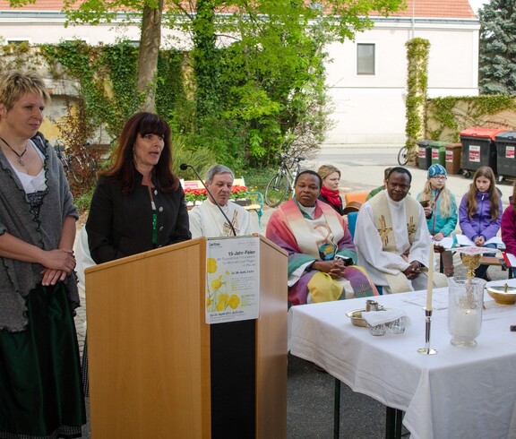 Eine Frau spricht ins Mikrofon, die anderen hören ihr aufmerksam zu.