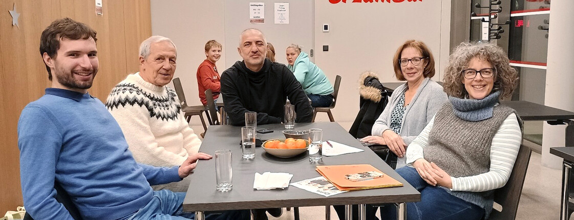Fünf Personen sitzen in einem Neubau an einem Tisch und schauen in die Kamera.