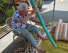 Eine Bewohnerin eines Pflegewohnhauses kühlt ihre Füße im Planschbecken und trainiert dabei spielerisch ihre Geschicklichkeit mit verschiedenen Wasserutensilien.