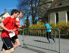 Zwei junge Burschen rennen in Sportbekleidung. Ein Junge hält Kopfhörer in seiner Hand. Gegenüber rennt ein Mann in die andere Richtung.