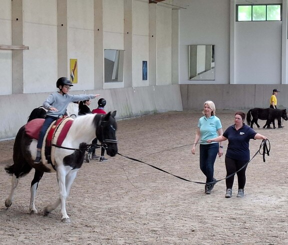 Reiter auf Pferd und zwei weitere Personen in der Reithalle 