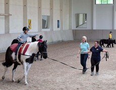 Reiter auf Pferd und zwei weitere Personen in der Reithalle 