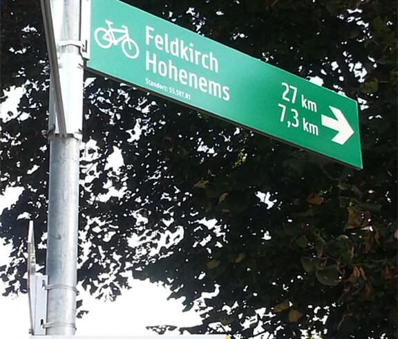 Ein grüner, und silberner Wegweiser wurde fotografiert. Sie weisen nach Feldkirch und Hohenems. 