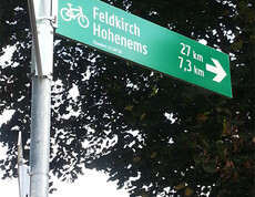 Ein grüner, und silberner Wegweiser wurde fotografiert. Sie weisen nach Feldkirch und Hohenems. 