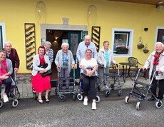 Bewohnerinnen und Bewohner eines Pflegewohnhauses haben gemeinsam einen Ausflug zu einem Weingut unternommen und stehen vor dem Gebäude für ein Gruppenfoto.