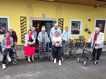 Bewohnerinnen und Bewohner eines Pflegewohnhauses haben gemeinsam einen Ausflug zu einem Weingut unternommen und stehen vor dem Gebäude für ein Gruppenfoto.