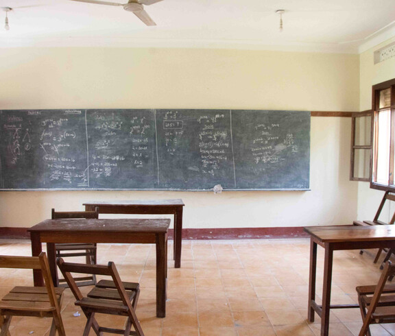 Leerer Klassenraum mit langer Kreidetafel voller Mathematikaufgaben, einfachen Holzschulbänken und einem Fenster – Unterrichtsraum des Caritas-Projekts Teaching Teachers im Südsudan.