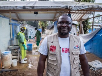 Ein Mitarbeiter der Caritas im Kongo. Er trägt ein weißes Shirt und eine beige Weste und blickt freundlich in die Kamera.