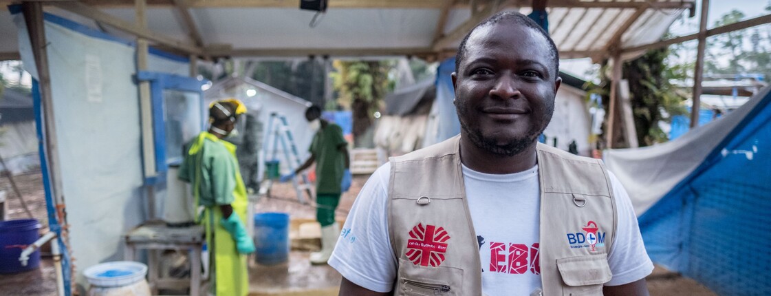 Ein Mitarbeiter der Caritas im Kongo. Er trägt ein weißes Shirt und eine beige Weste und blickt freundlich in die Kamera.