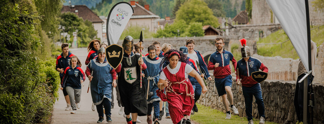 Gruppe läuft verkleidet und sportlich beim Caritas-Charity-Lauf mit Fahnen in bergiger Landschaft