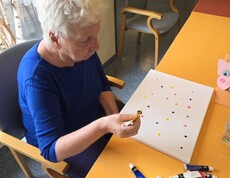 Eine weiter Bewohnerin des Pflegewohnhauses gestaltet konzentriert mit bunten Farbtupfern eine Leinwand und nimmt aktiv am kreativen Malangebot teil.