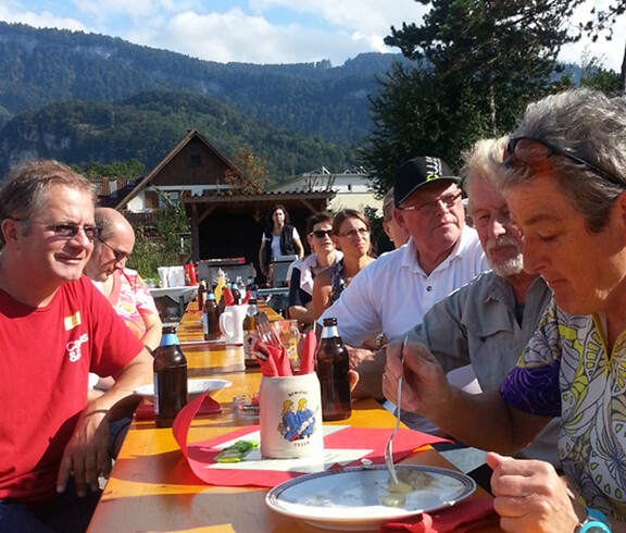 10 Personen sitzen an einem langen Biertisch und essen. Sie sind im Freien und haben es bei schönem Wetter gemütlich.  