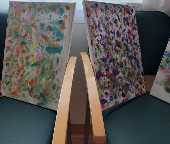 Mehrere bunt gestaltete Leinwände mit vielen Farbtupfern und abstrakten Mustern stehen nebeneinander und zeigen kreative Malarbeiten aus dem Alltag im Pflegewohnhaus.