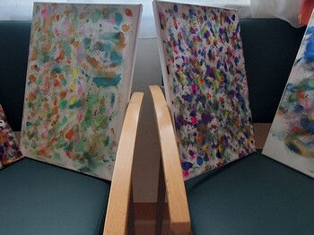 Mehrere bunt gestaltete Leinwände mit vielen Farbtupfern und abstrakten Mustern stehen nebeneinander und zeigen kreative Malarbeiten aus dem Alltag im Pflegewohnhaus.