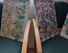 Mehrere bunt gestaltete Leinwände mit vielen Farbtupfern und abstrakten Mustern stehen nebeneinander und zeigen kreative Malarbeiten aus dem Alltag im Pflegewohnhaus.