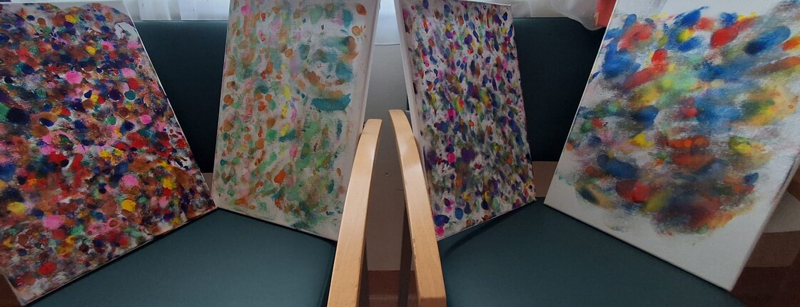 Mehrere bunt gestaltete Leinwände mit vielen Farbtupfern und abstrakten Mustern stehen nebeneinander und zeigen kreative Malarbeiten aus dem Alltag im Pflegewohnhaus.