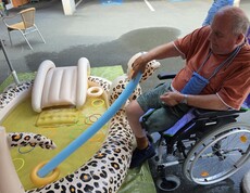 Ein Bewohner eines Pflegewohnhauses kühlt seine Füße im Planschbecken und trainiert dabei mit verschiedenen Wasserutensilien spielerisch seine Geschicklichkeit.