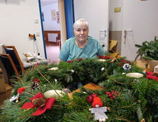 Großer Adventkranz mit roten Schleifen, Zapfen und kleinen Figuren auf Tisch