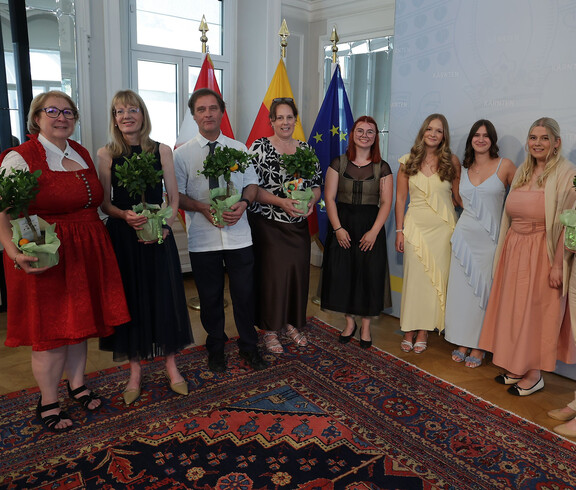 Gruppe von Erwachsenen mit Pflanzen in Händen vor Fahnen von Kärnten und EU