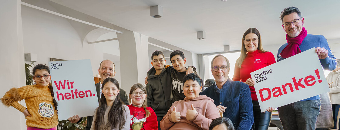 Gruppe im Lerncafé mit Schildern „Wir helfen.“ und „Danke!“ bei Spendenübergabe