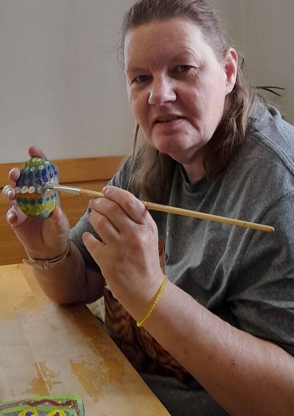 Frau sitzt an Tisch und malt Stein