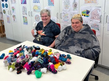 Zwei Frauen vor einem Berg selbst gestrickter oder gehäkelter Mützchen.