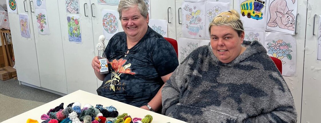 Zwei Frauen vor einem Berg selbst gestrickter oder gehäkelter Mützchen.