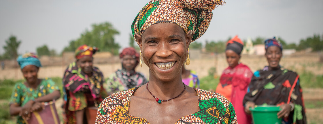 Eine Frau mit buntem Kleid und Kopftuch steht vor einem Bewässerungsbrunnen in der Region Kayes in Mali.