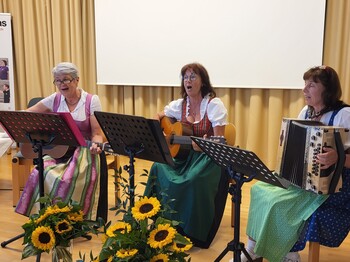 Drei Frauen sitzen und spielen Musikinstrumente, zwei Gitarren und eine Harmonika.