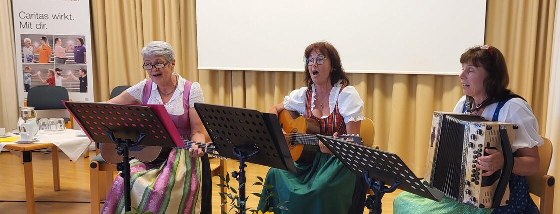 Drei Frauen sitzen und spielen Musikinstrumente, zwei Gitarren und eine Harmonika.