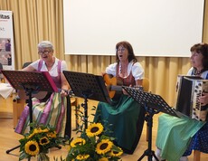 Drei Frauen sitzen und spielen Musikinstrumente, zwei Gitarren und eine Harmonika.