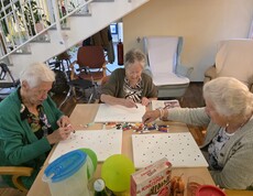 Drei Bewohnerinnen des Pflegewohnhauses sitzen gemeinsam am Tisch und gestalten mit bunten Farben kreative Punktbilder auf Leinwänden.
