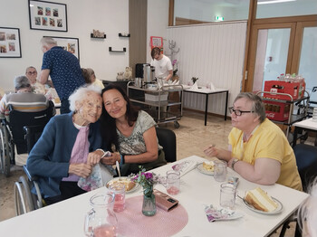 Eine Angehörige umarmt eine Bewohnerin liebevoll an einem gedeckten Tisch mit Torte, Getränken und Blumen.