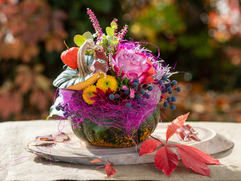 Herbstliches Arrangement aus Kürbis, Blumen und Beeren auf einem Tisch.