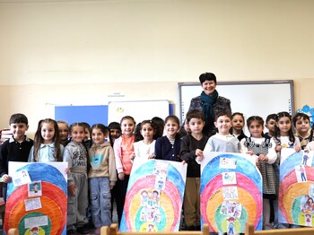 Eine Frau steht in einem Klassenzimmer in Armenien hinter einer großen Gruppe an Schulkindern, die selbstgemalte Plakate präsentieren.