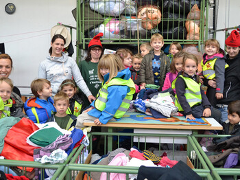 Kindergartenkinder sind zu Besuch beim carla Sortierwerk. Sie stehen neben bzw. sitzen auf den Wägen, in dem sich das sortierte befindet. Manche Kinder tragen eine gelbe Warnweste. 