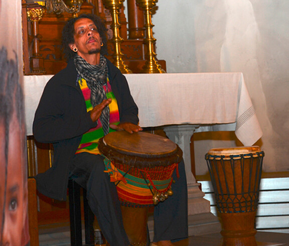 In der Pfarrkirche von Frastanz spielt ein Afrikaner Trommel. Er ist komplett in Schwarz gekleidet. 