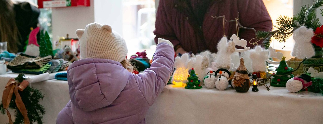 Kleines Mädchen übernimmt auf einem Weihnachtsmarkt ein Produkt von einer Frau