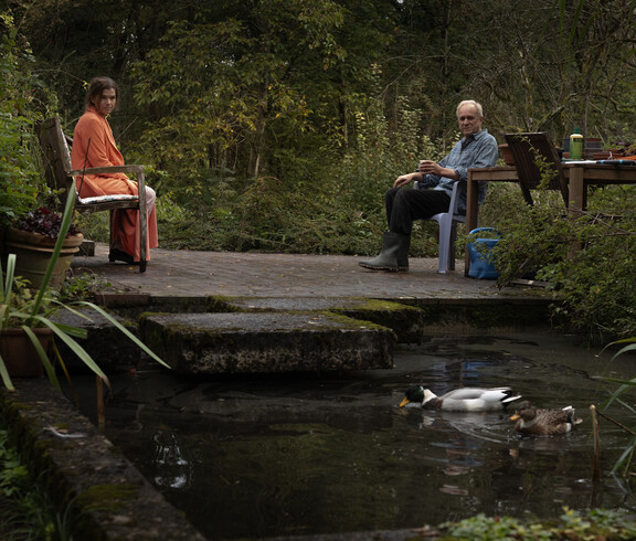 Frau und Mann sitzen im Garten, davor schwimmt eine Ente im Teich