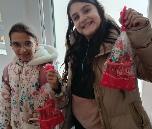 Zwei Kinder zeigen fröhlich ihre Nikolausgeschenke in die Kamera.