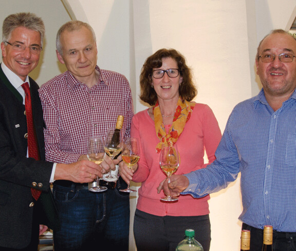 Vier Personen lächeln mit einem Glas Wein in der Hand in die Kamera