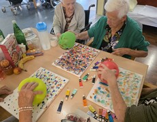 Mehrere Bewohnerinnen des Pflegewohnhauses experimentieren kreativ mit Farben und Luftballons, um lebendige und farbenfrohe Kunstwerke auf Leinwänden zu gestalten.
